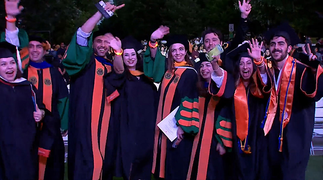 Graduates in regalia waving at University Commencement