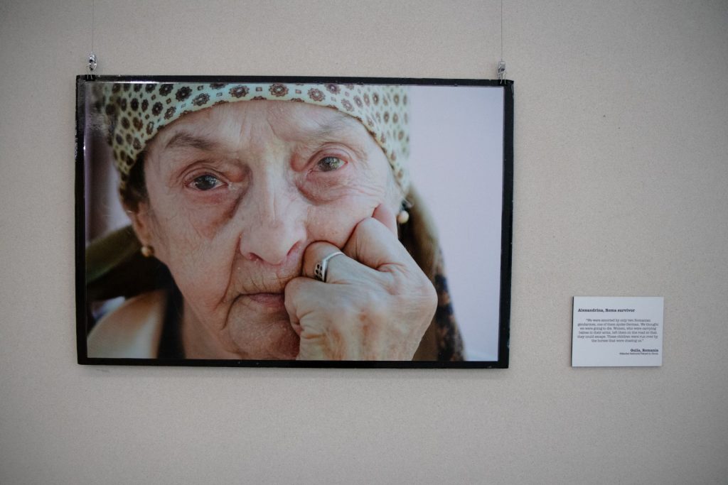 An elderly woman's portrait displayed on a wall, part of an exhibition on genocidal practices from World War II until today.