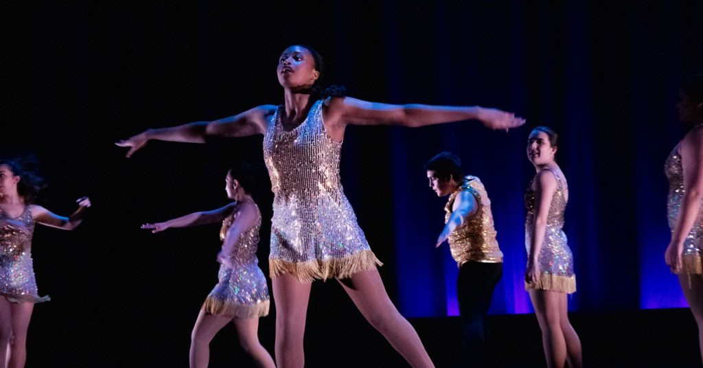 Dancers in gold dresses perform on stage during the Spring 2024 Dance Collections concert by UTDance Ensemble and other collaborators.