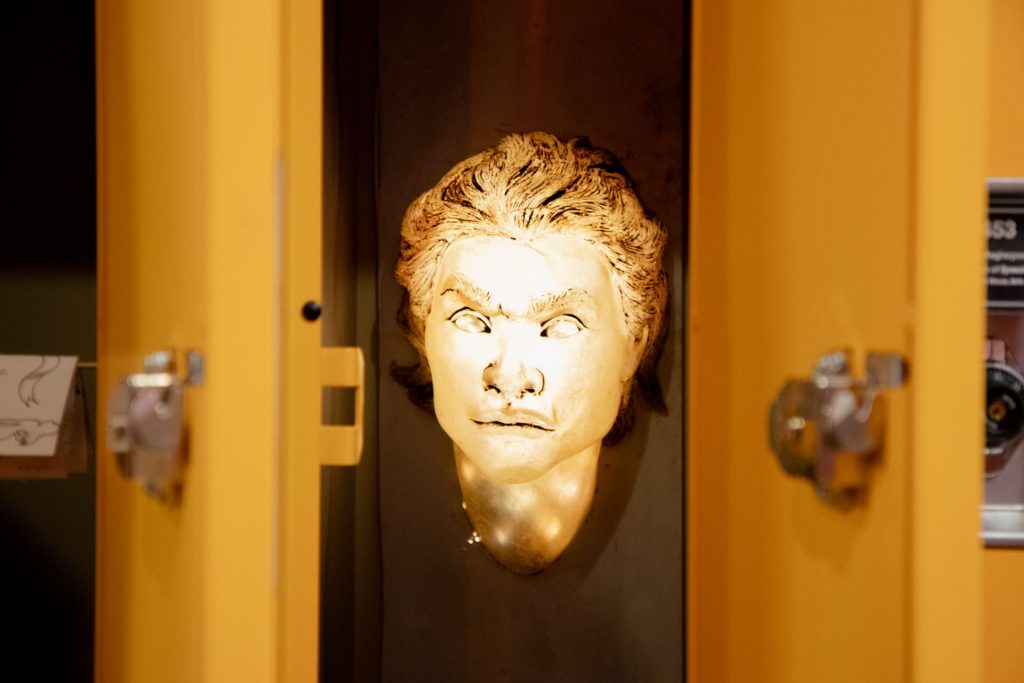 Holly Havens' art piece: gold mask on locker wall, representing struggles with religion and journey to self-acceptance.