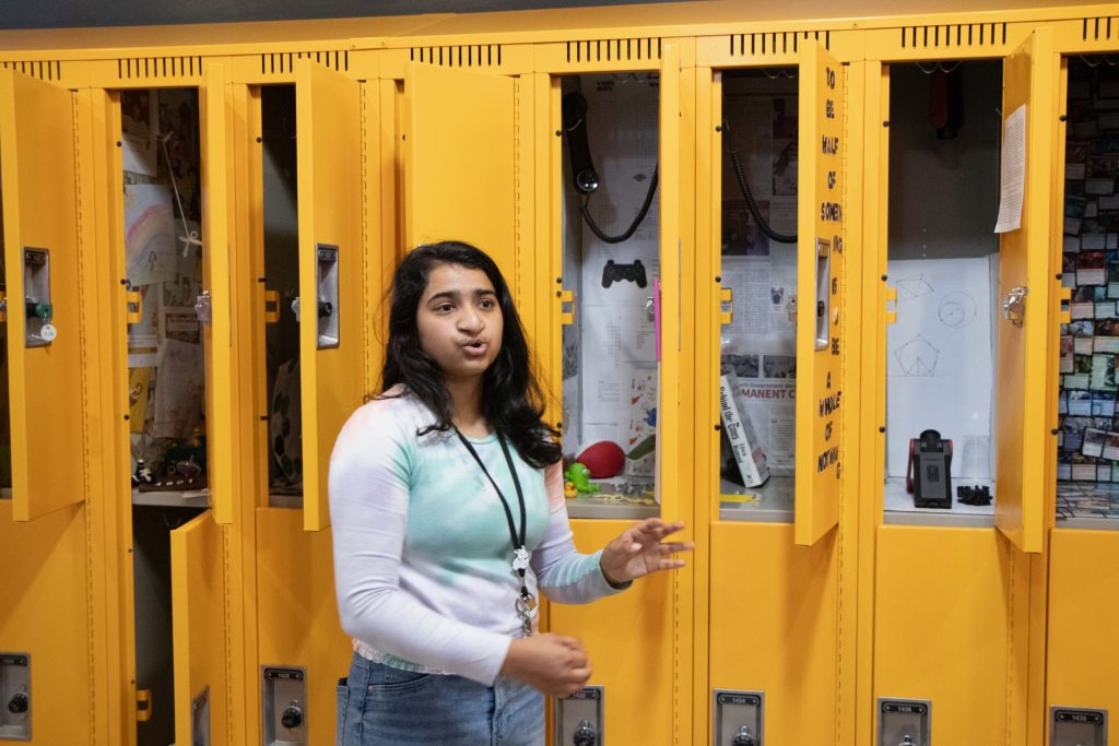 Amulya Prasad Rayabhagi stands before yellow lockers, representing the contrasting characters of Sam and Sadie in "Tomorrow, and Tomorrow, and Tomorrow". The lockers symbolize their distant yet existing connection, with pebbles denoting the years passed and books reflecting their personalities. The woman's locker showcases a crocheted yarn, symbolizing their fragile yet enduring friendship.
