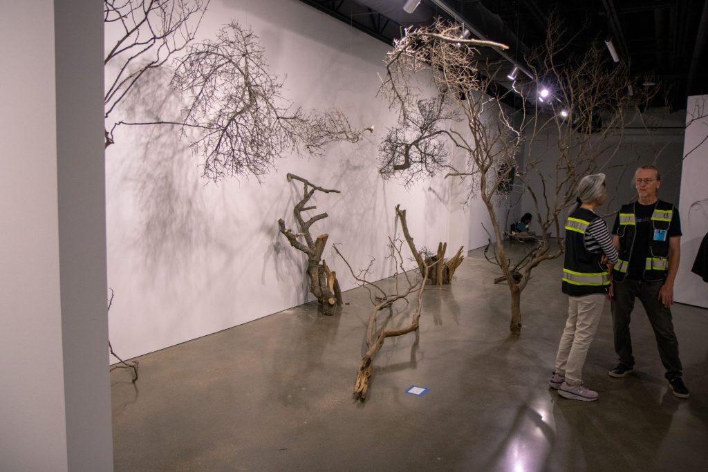 Two people standing in front of a tree sculpture in an art exhibit.